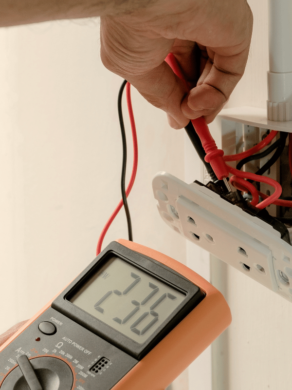Electrician testing wiring behind an outlet with a multimeter